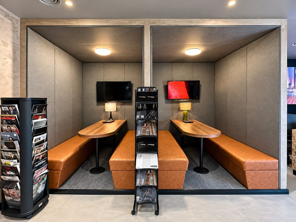 Two upholstered client meeting booths with wall TVs and brochure racks at Metroplus head office