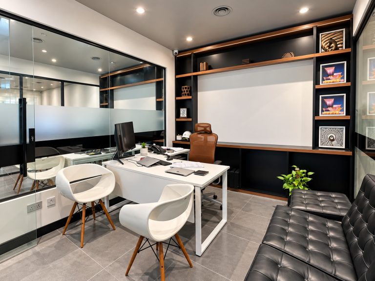 Managing director office with glass partition, shelving and Barcelona-style sofa at Metroplus head office