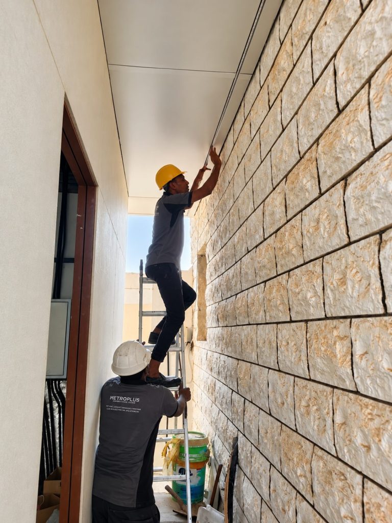 Metroplus installers fixing ceiling panels along a stone-clad corridor